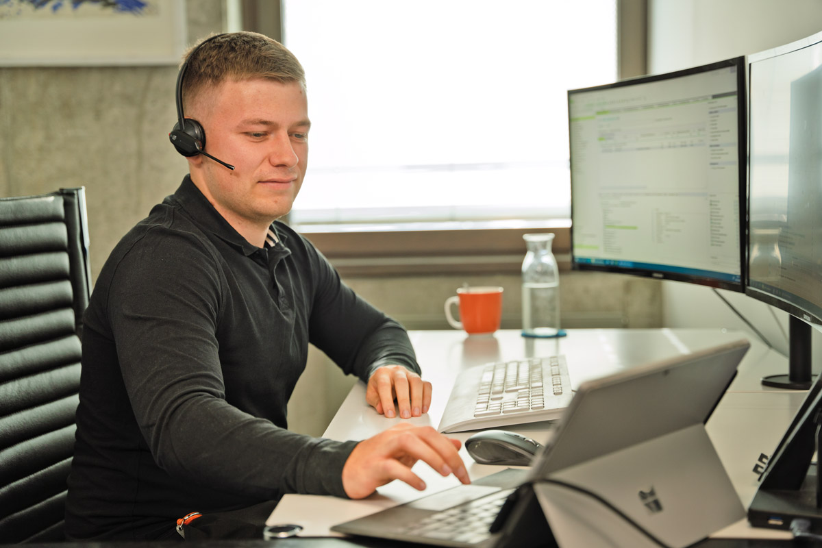 Taxellenz-Mitarbeiter in Arbeitssituation am Computer mit Headset.